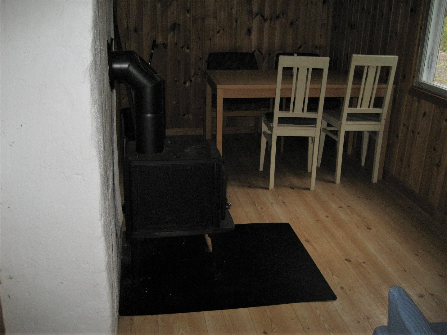 Vit murstock och kamin till vänster. Längst in i rummet står ett bord med fyra stolar.