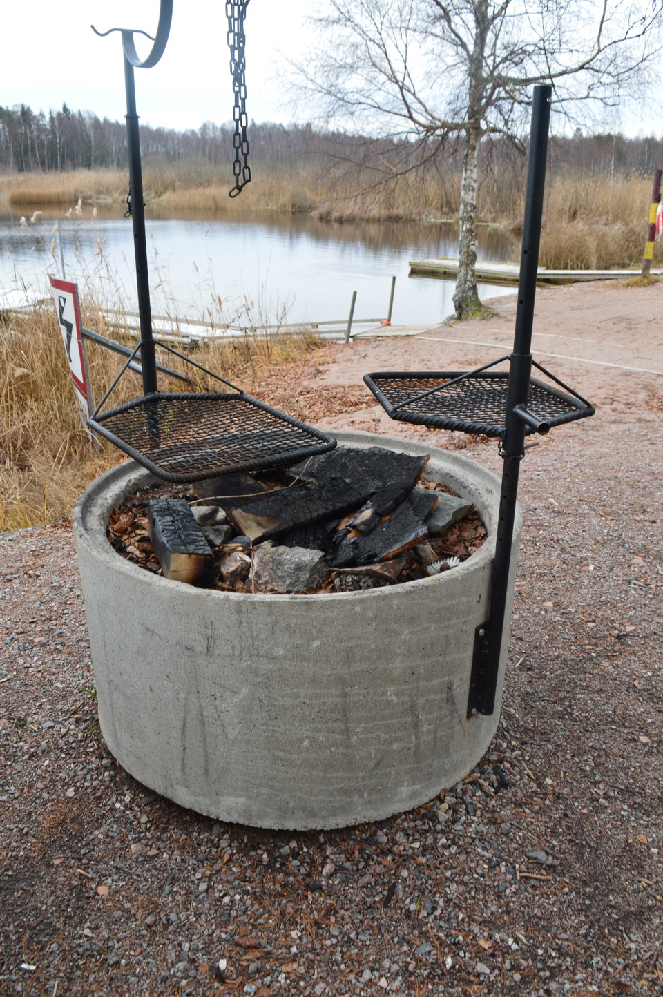 Närbild på en grillplats. Två grillgaller finns över grillen och inne i grillen ligger förkolnat ved.