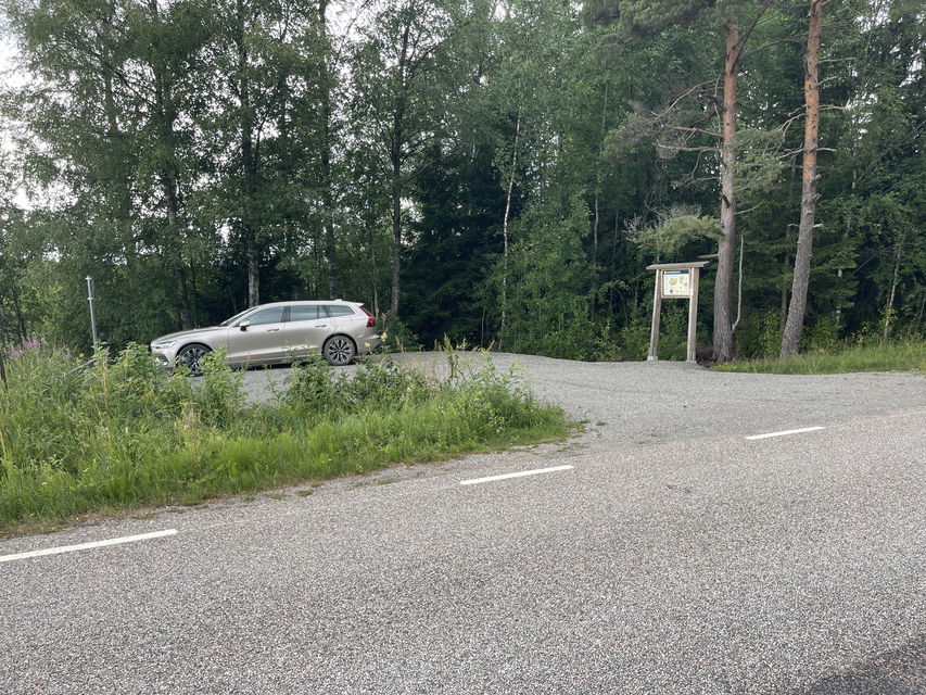 Parkering vid sidan av en landsväg. En informationstavla finns vid parkeringen. En bil står parkerad.
