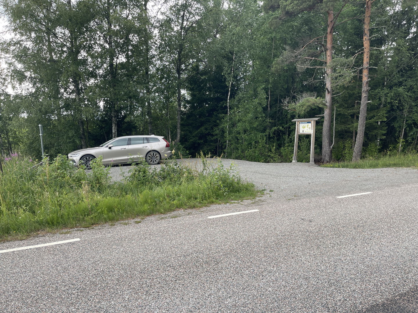 Parkering vid sidan av en landsväg. En informationstavla finns vid parkeringen. En bil står parkerad.