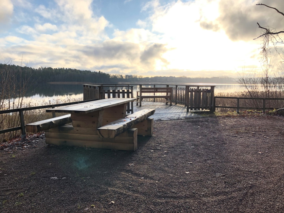 Ett bänkbord står på ett grusplan. I balgrunden står utsiktsplattform med högt staket runtom.