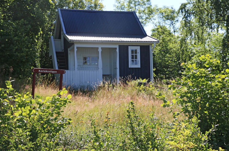 En röd skylt med text Kärleksstigen framför ett rött torp.