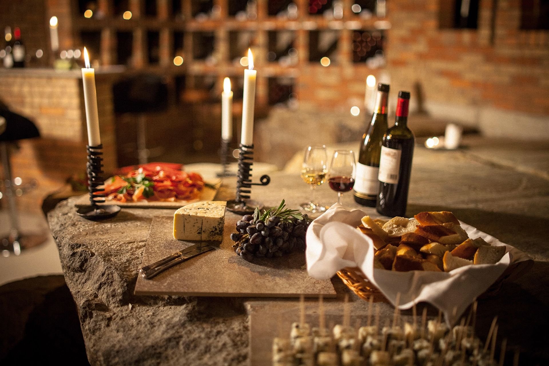 Vinflaskor och ostar på ett bord i en källare.