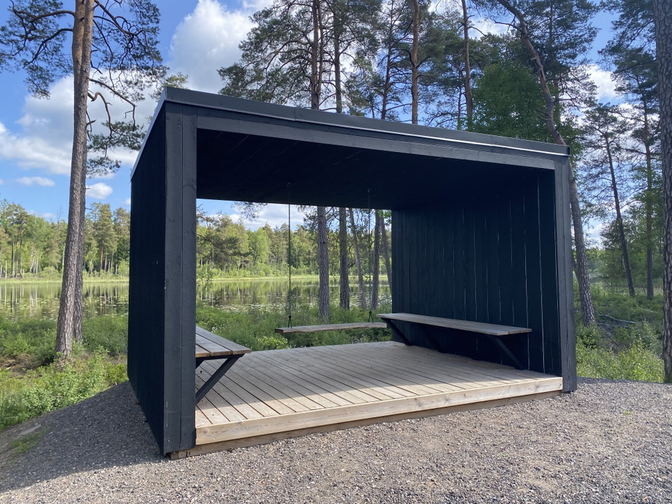 Ett vindskydd med skog och sjö i bakgrunden.