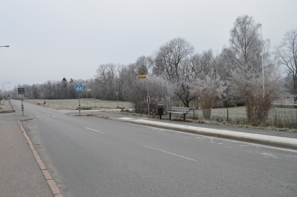 En busshållplats vid sidan av en bilväg. På hållplatsen finns en sittbänk.