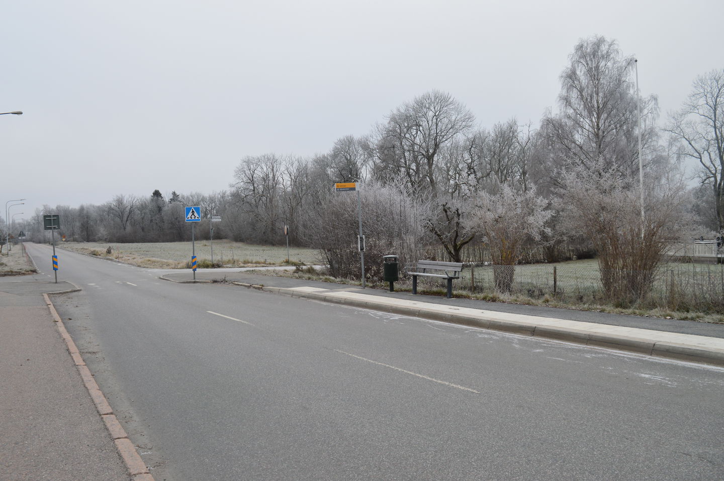 En busshållplats vid sidan av en bilväg. På hållplatsen finns en sittbänk.