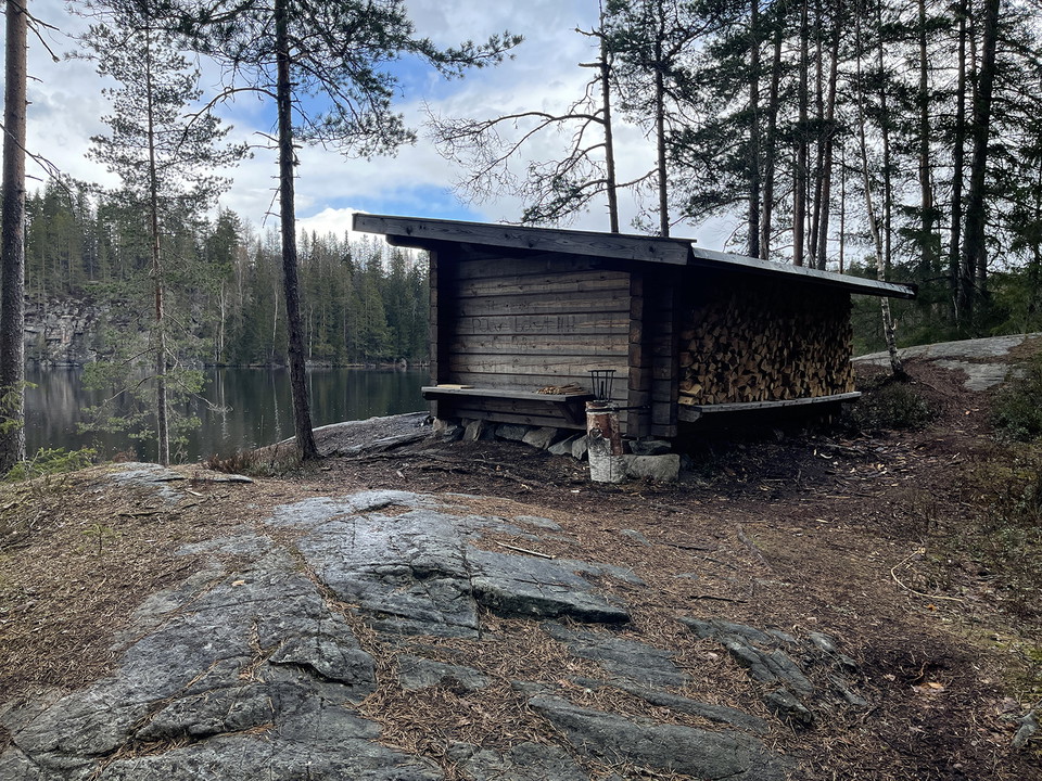 Vindskydd i knuttimmer. Det finns ved och en huggkubb bredvid.