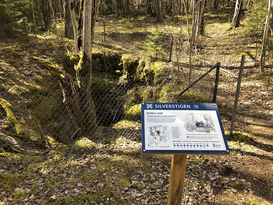 Informationstavla vid inhägnat hål i marken.