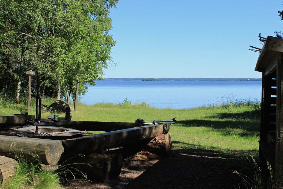 En låg grillplats med sittbänkar runtom står på en gräsyta vid vattnet.