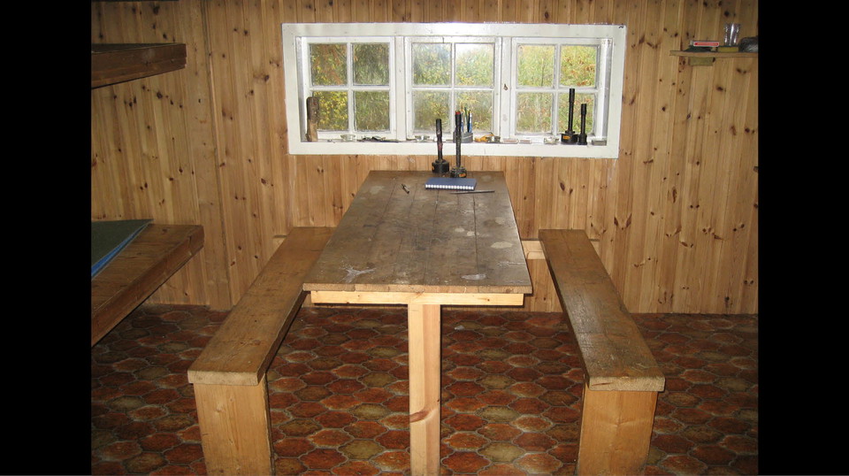 Inne i stugan: fasta bänkar och bord vid fönster.