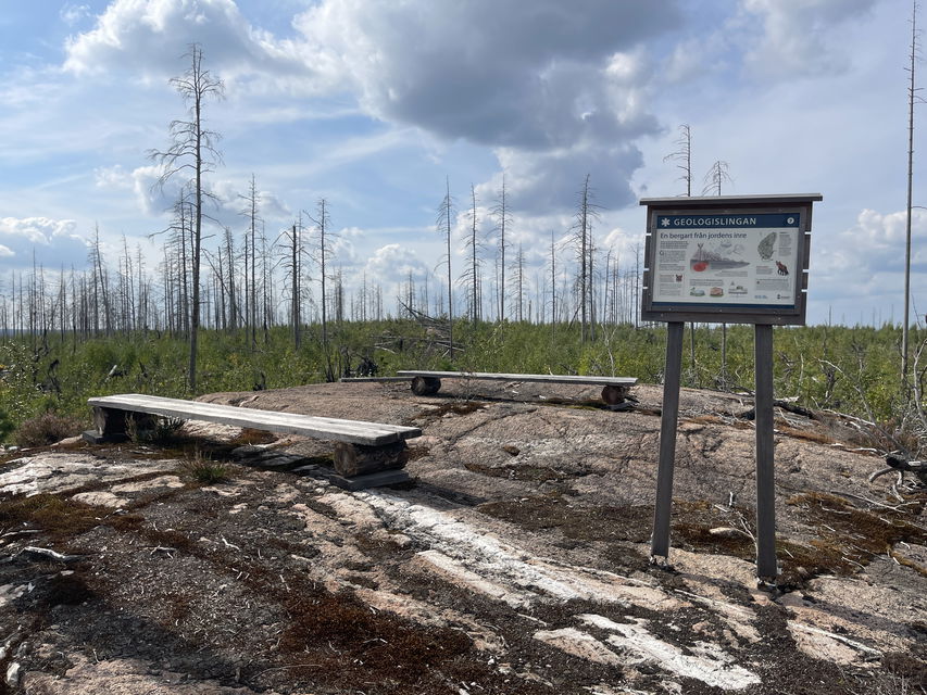 Informationsskylt vid stig, om geologi. Två enkla bänkar står bredvid.