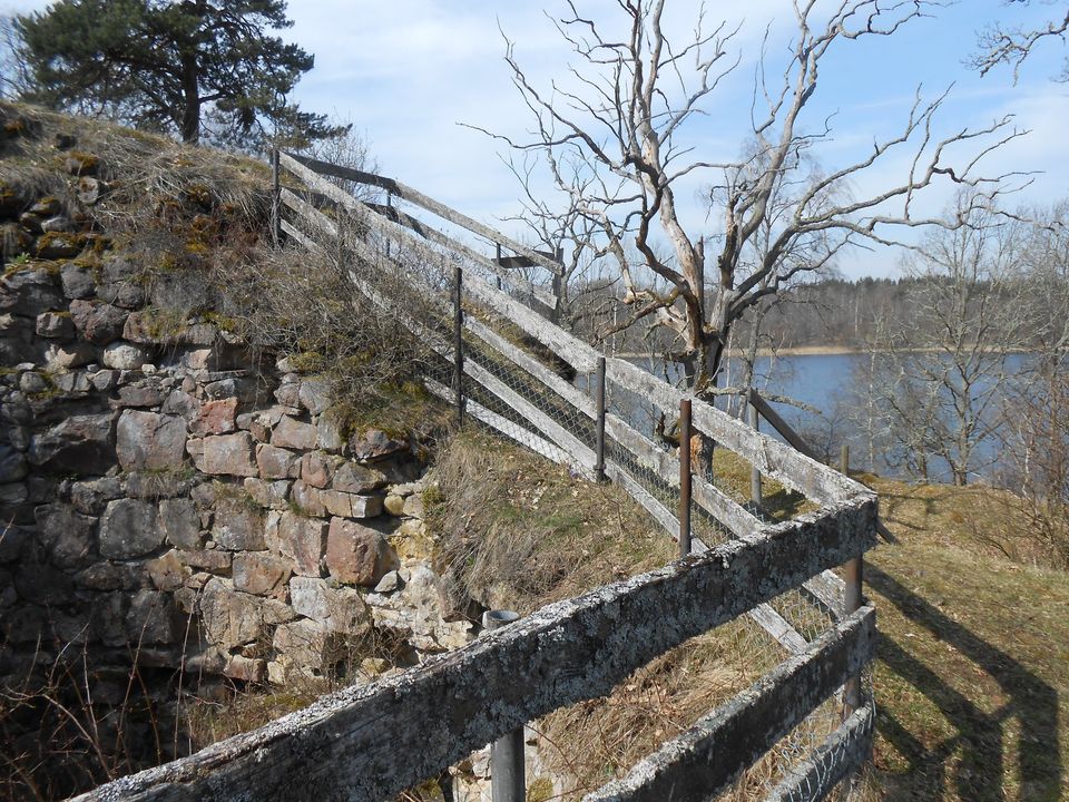 Borgruin med trästaket runt och utsikt över sjö