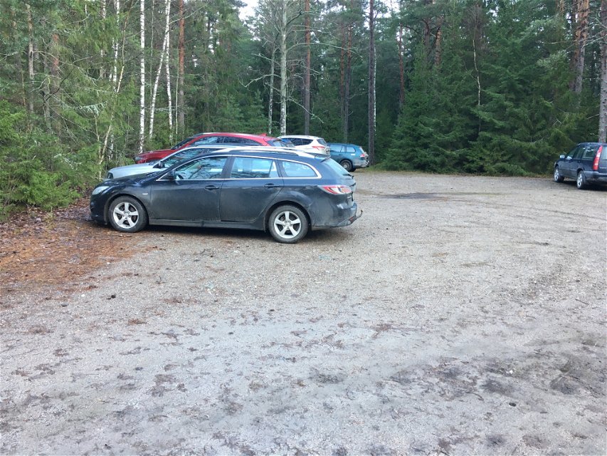 En grusplan omgiven av skog och sex bilar som står parkerade längs kanten.