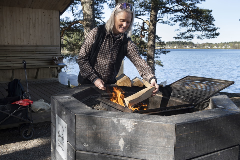 Kvinna lägger på ett vedträ på elden i eldstaden på Kalvaberget.