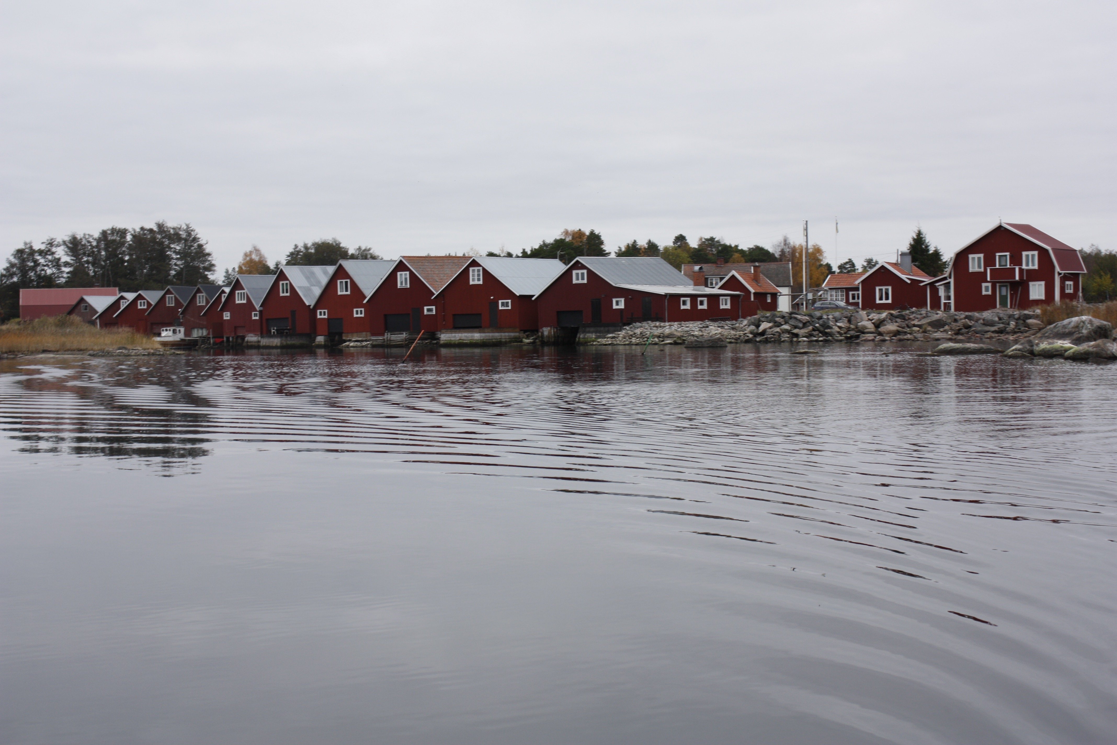 Vid vattenbrynet står flera båthus på rad bredvid varandra. Bakom dem står flera bostadshus och bodar.