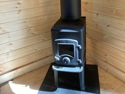 Svart gjutjärnskamin i ett hörn av stugan.