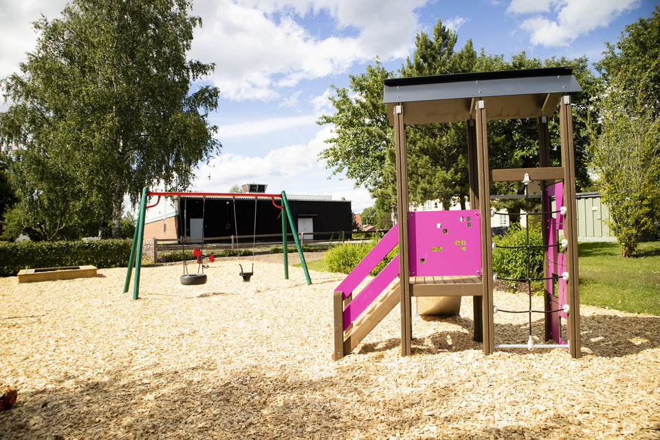 Litet hus med rutschkana och klätterställning med gungor i bakgrunden
