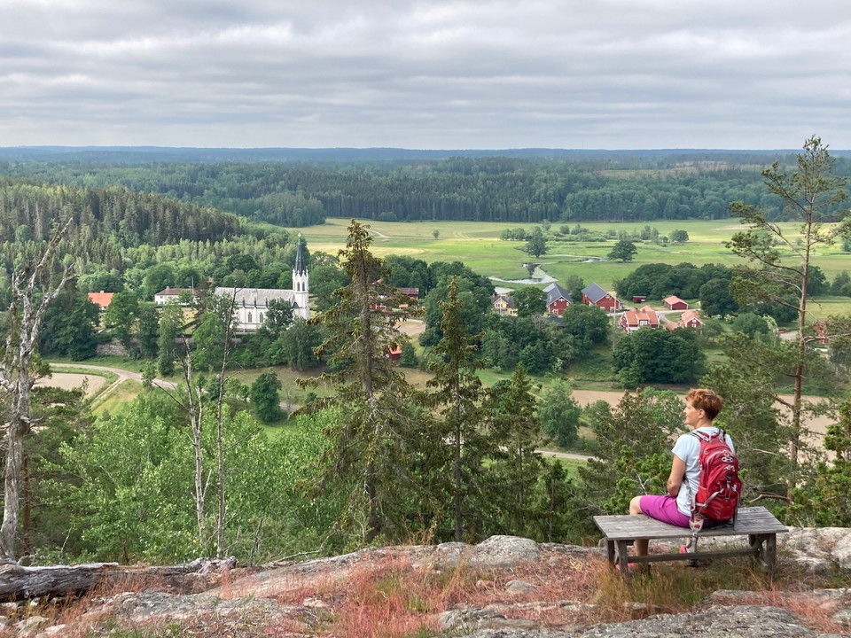 En kvinna sitter på en bänk och tittar ut över en dalgång