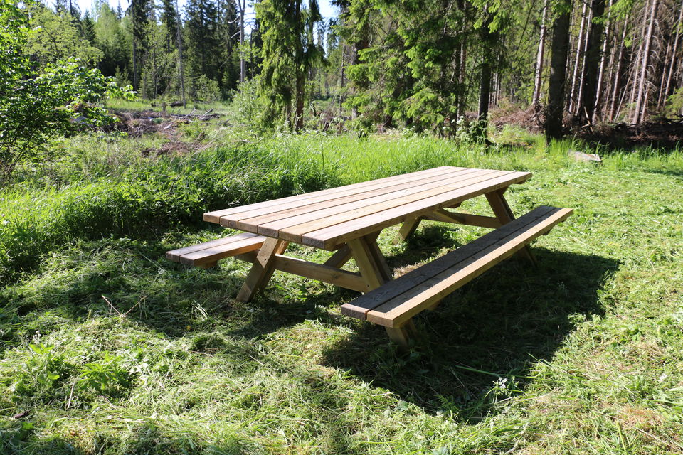 Ett picknickbord som står på gräs, träd i bakgrunden.