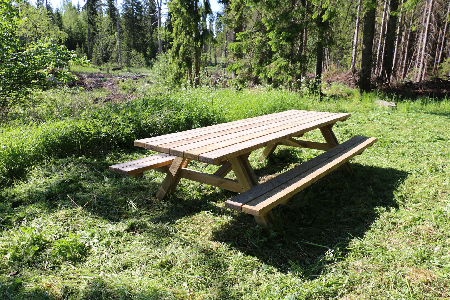 Ett picknickbord som står på gräs, träd i bakgrunden.