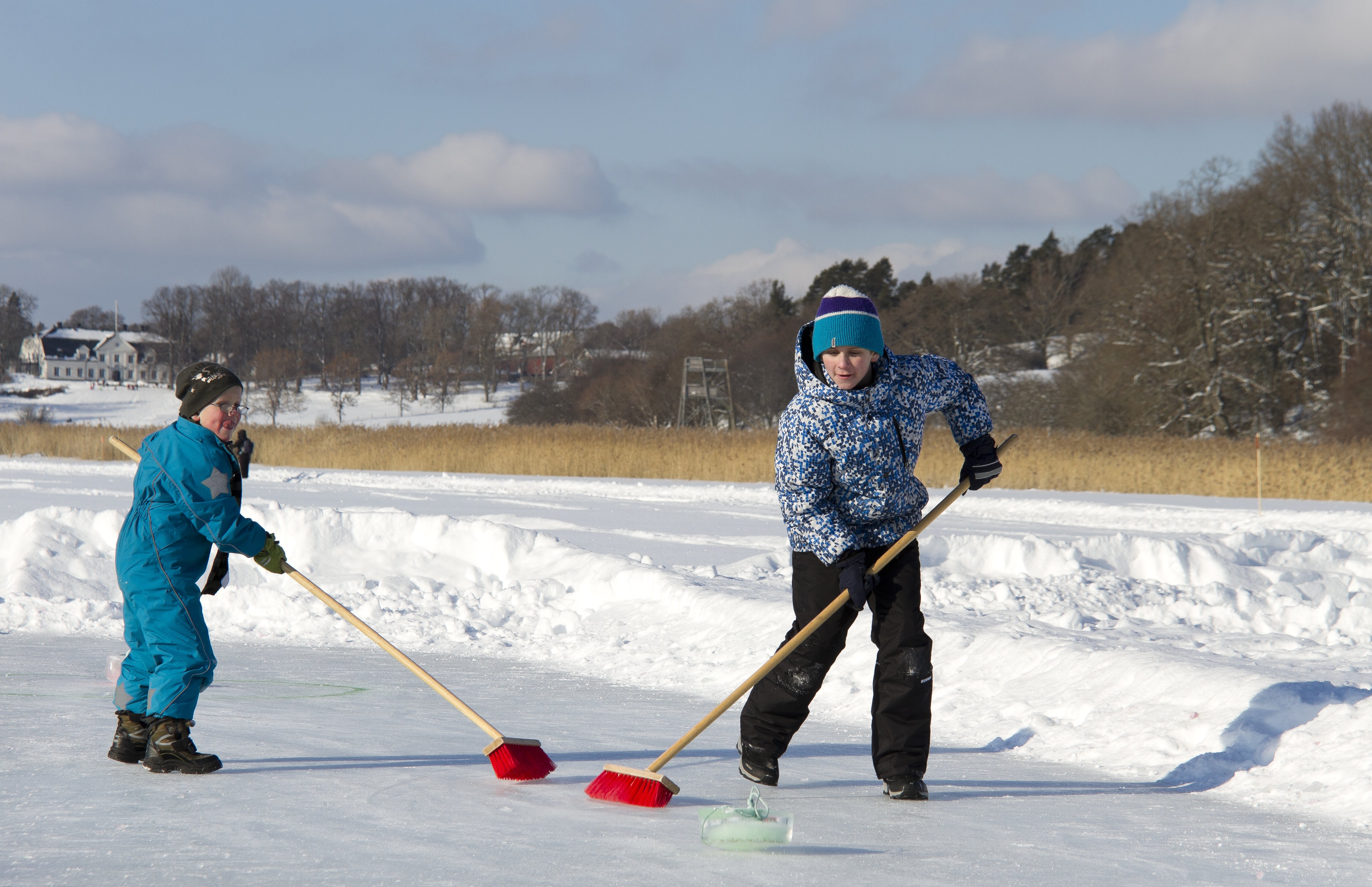 Två barn spelar curling med sopkvastar.