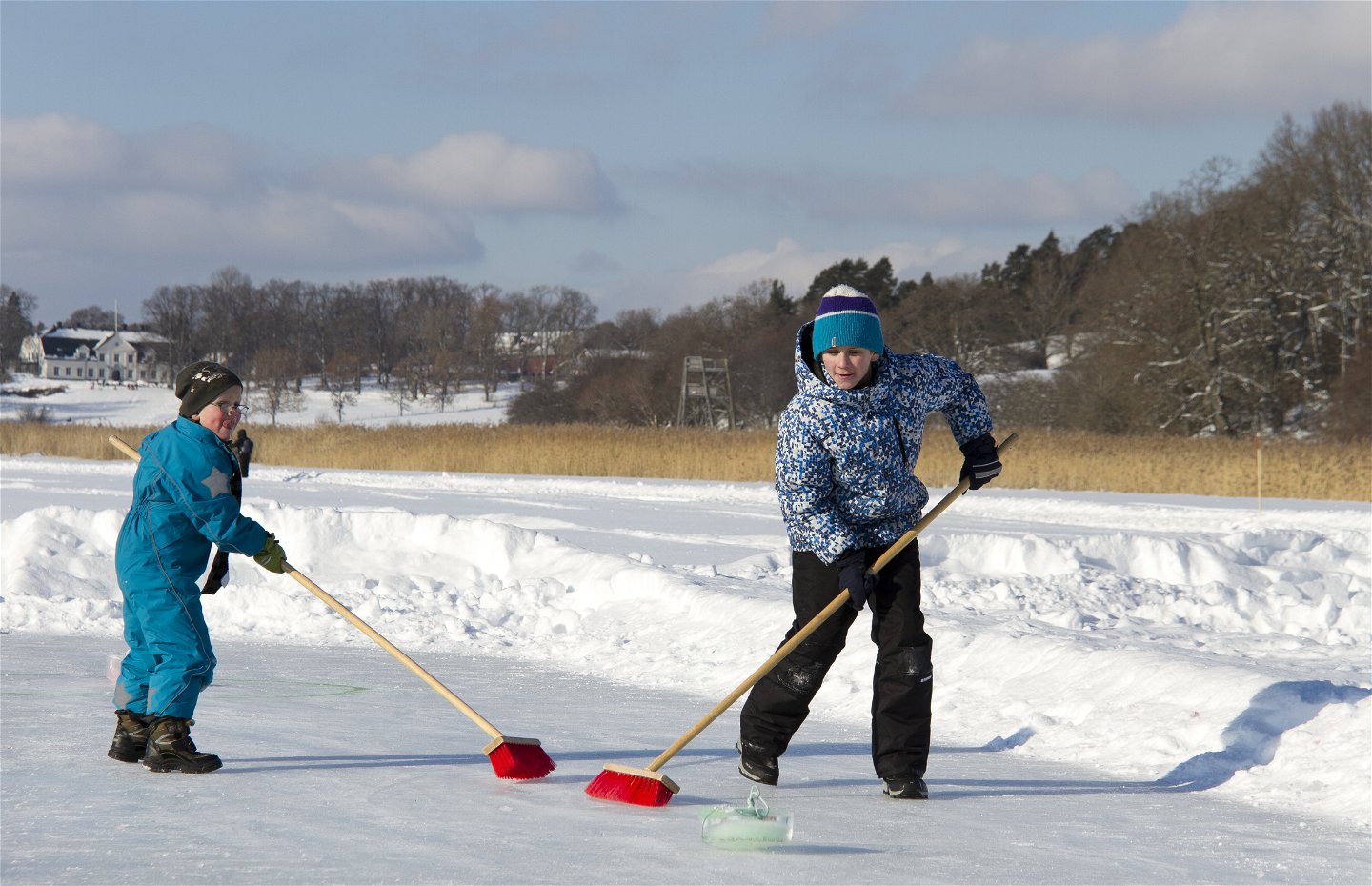 Två barn spelar curling med sopkvastar.