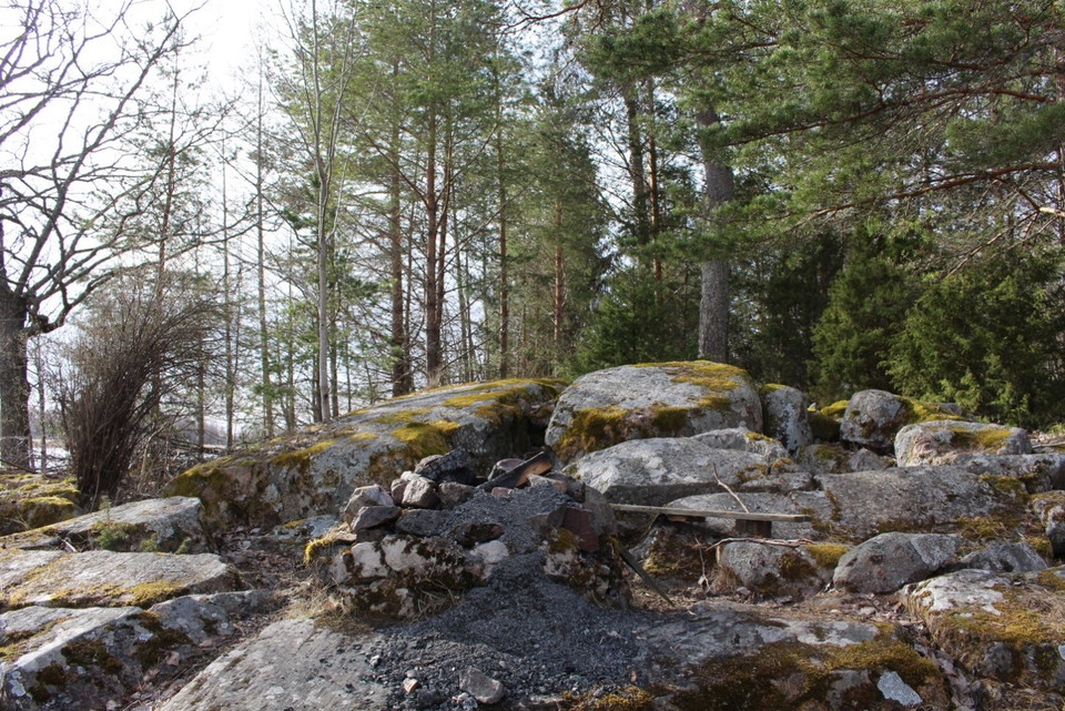 Bland stora stenblock finns en grillplats med en sittbänk bredvid.