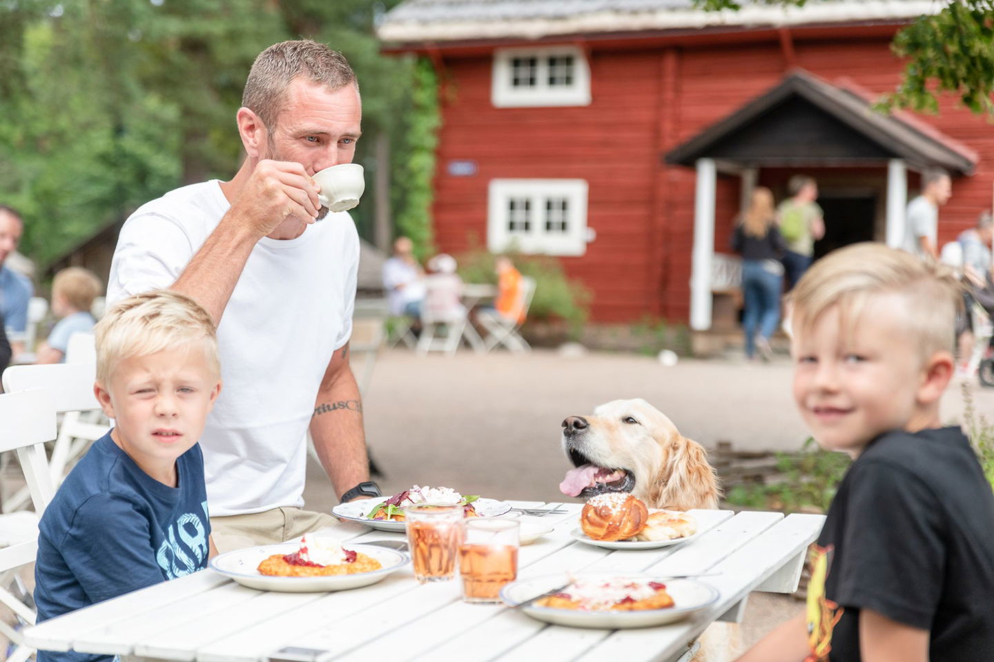 Pappa, två pojkar och en hund fikar på våffelkaféet Spikgårdens uteservering.