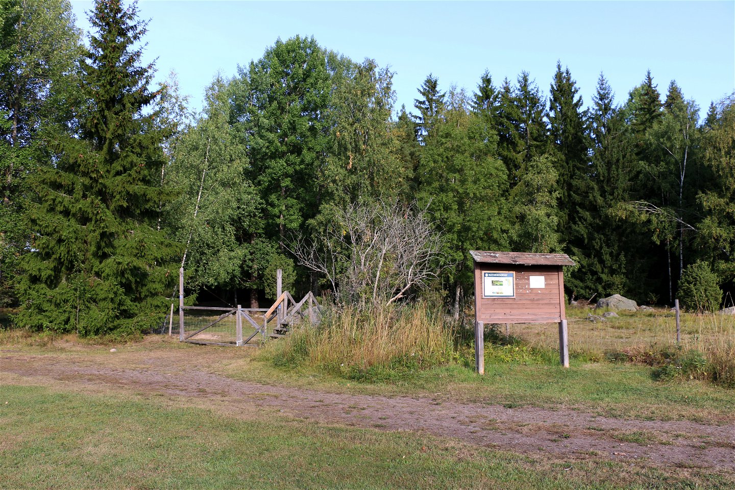 Informationstavlan invid staket med övergång in till naturreservatet.