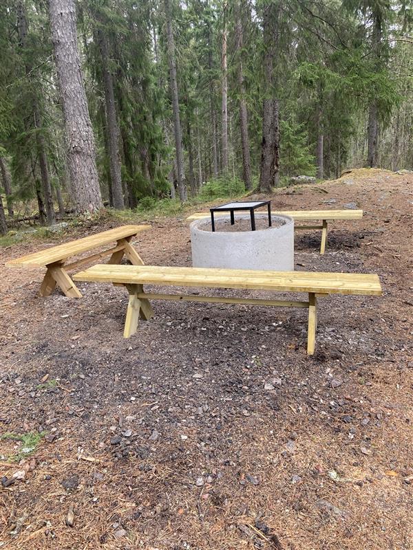 Rastplats med tre sittbänkar och eldstad i mitten i fin skogsmiljö