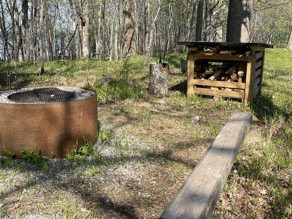 Rund eldstad med galler. Vedförråd och en enkel bänk.