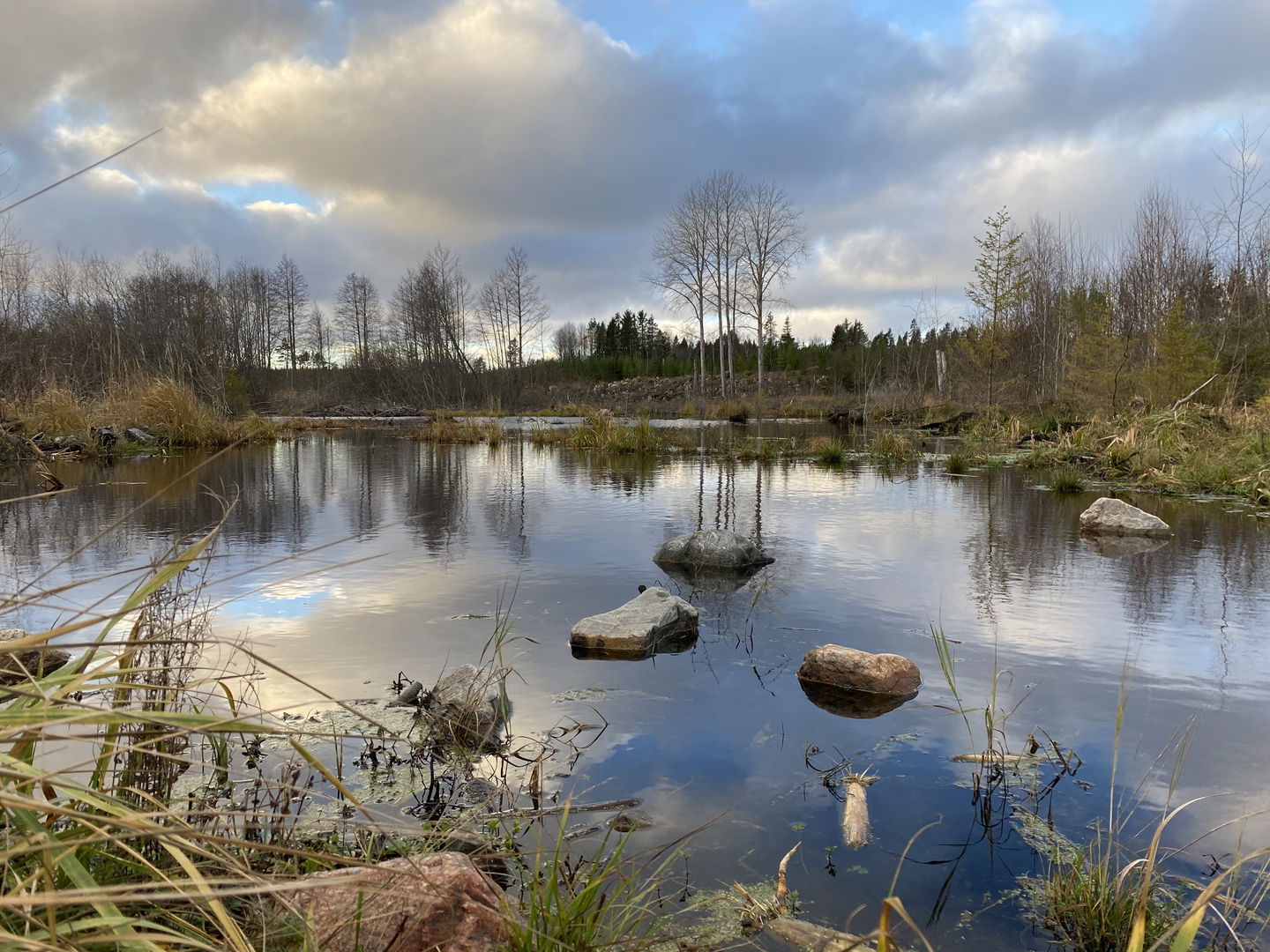 Litet vatten med stenar i. Himlen speglar sig i vattnet.