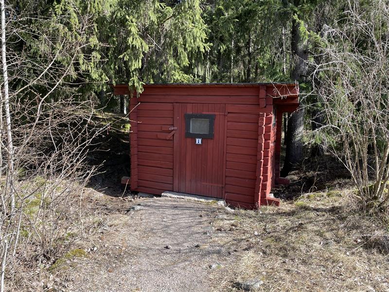 En röd dassbyggnad med WC symbol 