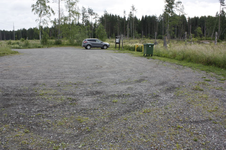 En stor grusplan med vägbom ned mot vattnet. En informationsskylt står vid parkeringens kant.
