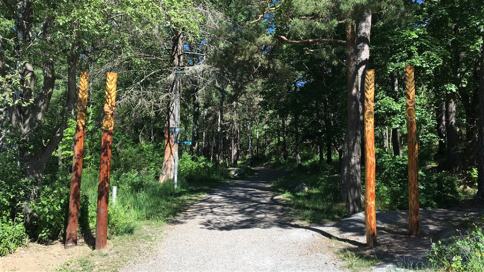 Utsmyckade trästolpar invid en grusad väg i en skog.