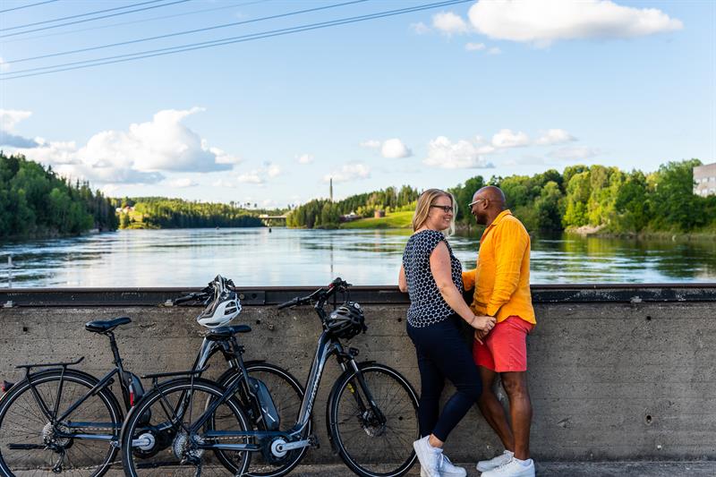 Ett par på sykkeltur tar seg en pause ved vannet på oversiden av kraftstasjonen på Kykkelsrud