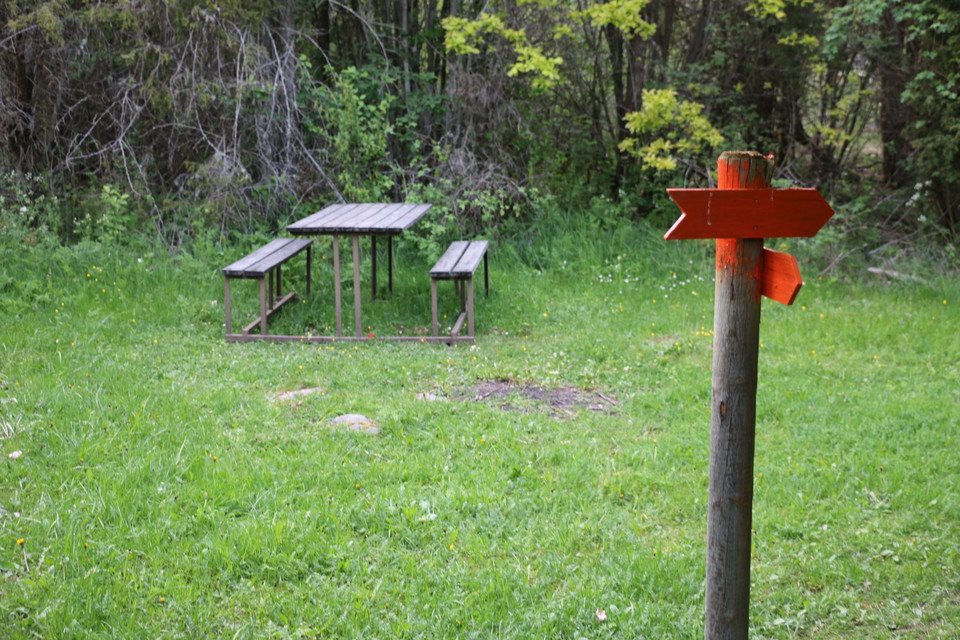 Ett bord med bänkar står längs leden. Orange pilar på en stolpe visar vägen.