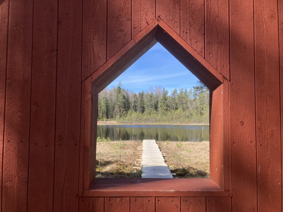 En brygga i en liten sjö som syns genom en glugg i en trävägg