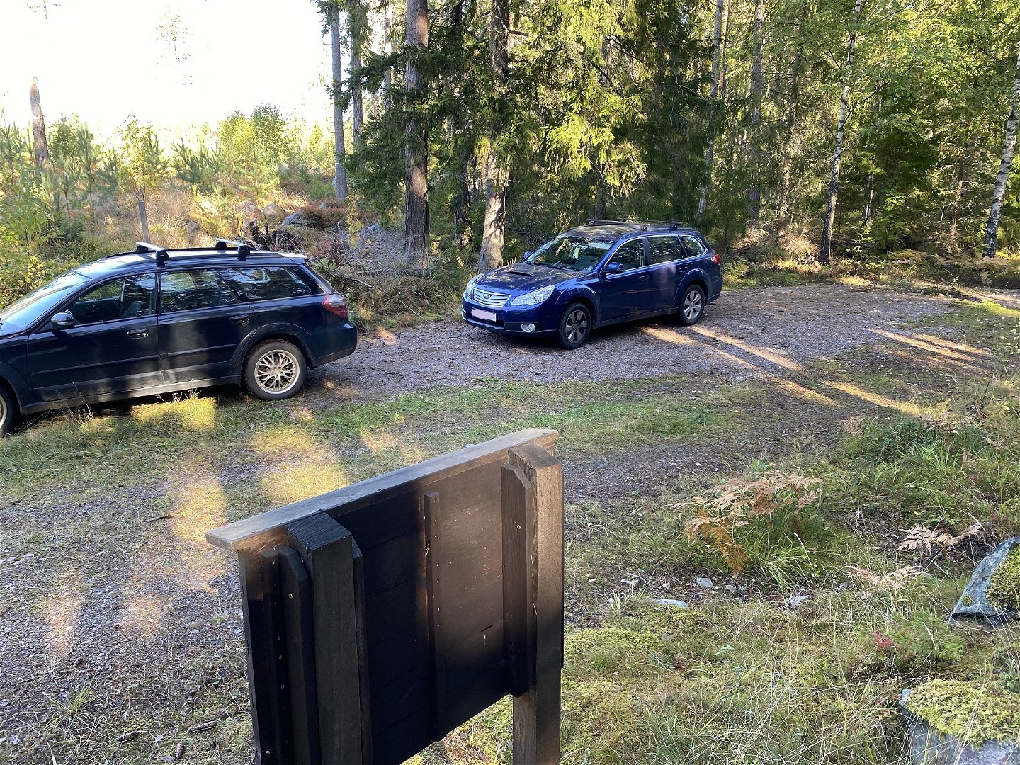 Två bilar står på rad på en grusad yta. I förgrunden syns baksidan på ett skyltställ.