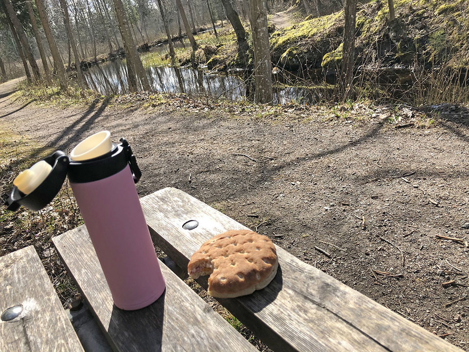 Rosa lite termos och dubbelsmörgås på en bänk i vårsol.
