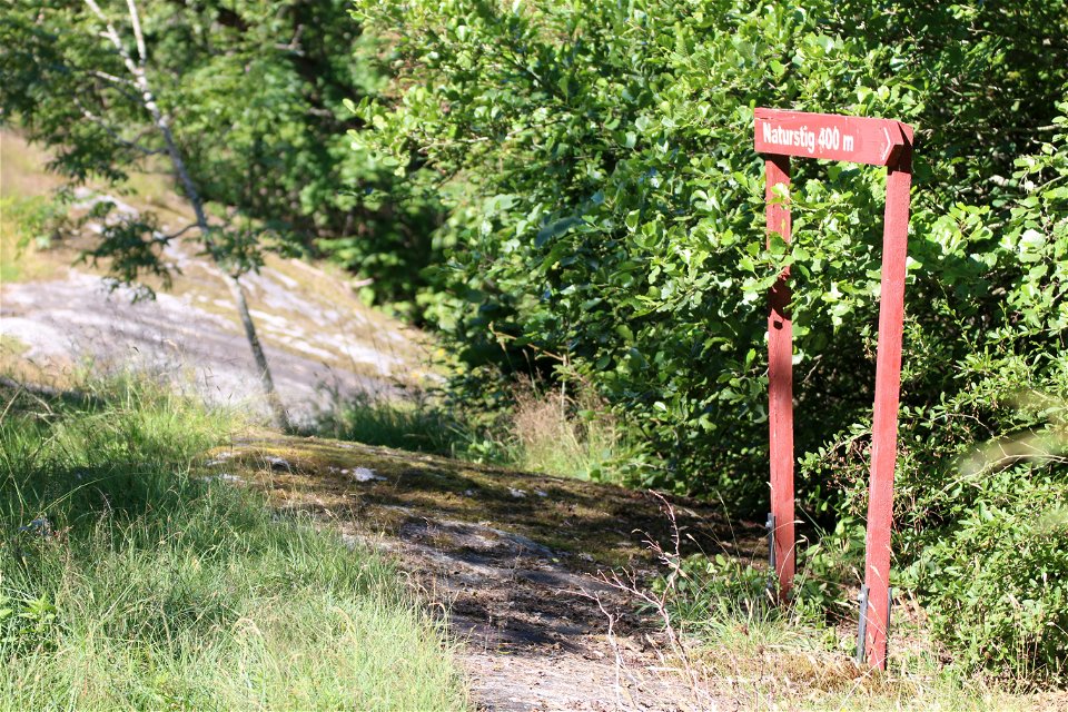 På en klipphäll står en röd träskylt med text Naturstig 400 meter och visar vägen.
