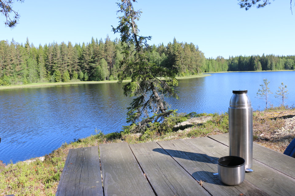 Ett träbord med en termos som står på en klippa i en skog med en sjö i bakgrunden.