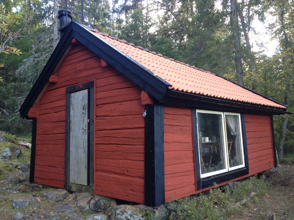 En liten stuga med stort fönster står i skogen.