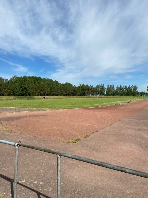 Fotbollsplan med naturgräs och löparbanor med grus i form av röd kolstubb