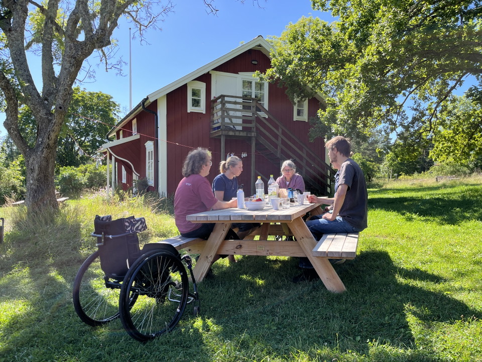 Ett rastbord med flera personer som fikar, en av dem har en rullstol bredvid sig.