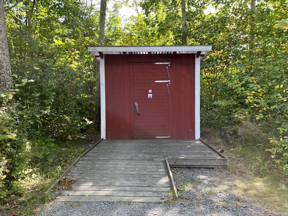 En bild på litet rött hus med vita knutar och ramp upp.