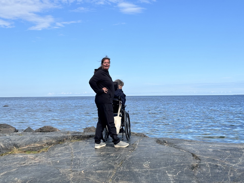 En kvinna i rullstol med assistent blicka rut över havet.
