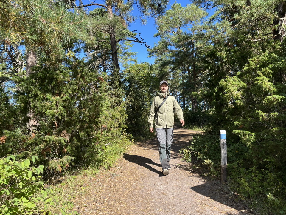 En man kommer gående på en bred grusad stig genom skogen.