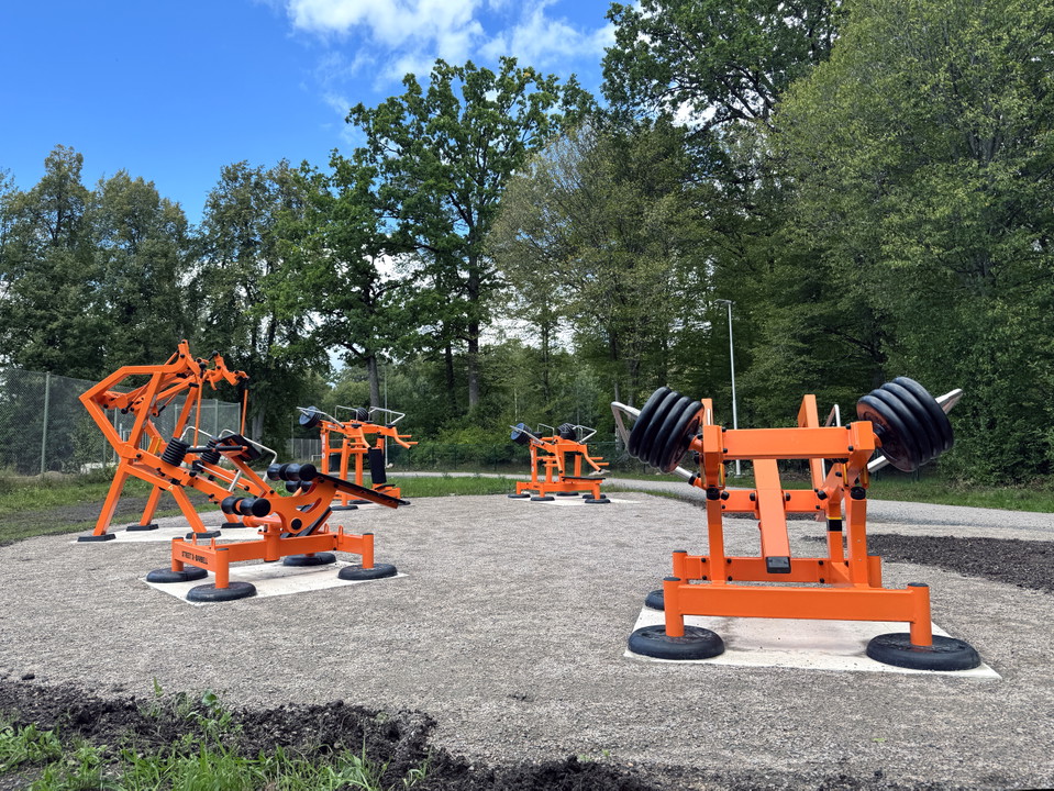 Fem träningsmaskiner står i grupp. Maskinerna är i orange metall.