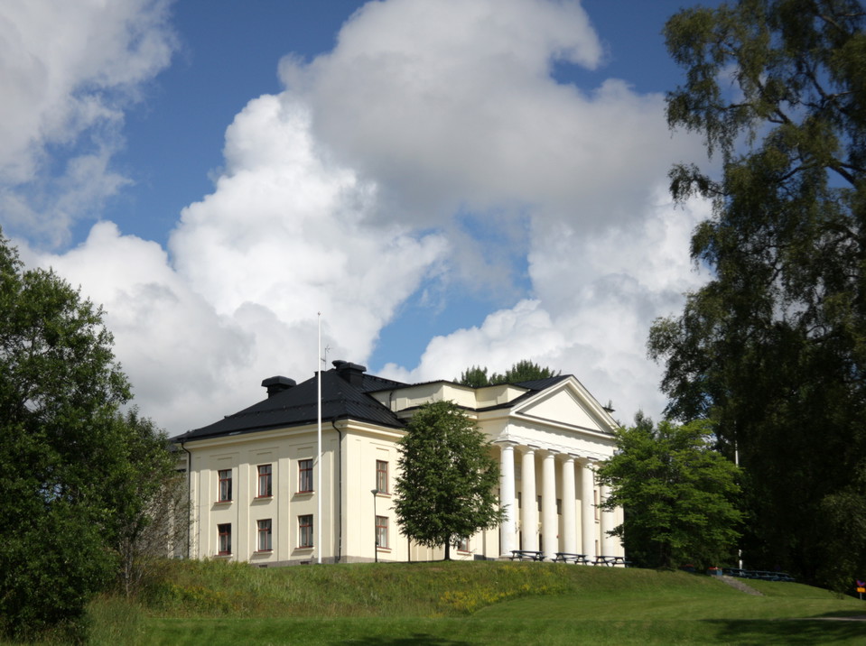 Bild på vitt hus med vita pelare. Huset står på en grönskande kulle. 
